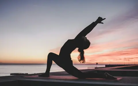 A person stretching on an outdoor mat at sunset